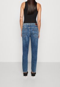 Blue denim jeans with a straight-leg cut, featuring two back pockets and a leather tag at the waistband. Worn with black shoes.