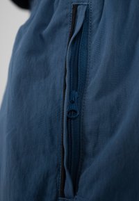 Nahaufnahme eines blauen Stoffreißverschlusses mit einer teilweise geöffneten Tasche, die detaillierte Nähte und Textur zeigt.