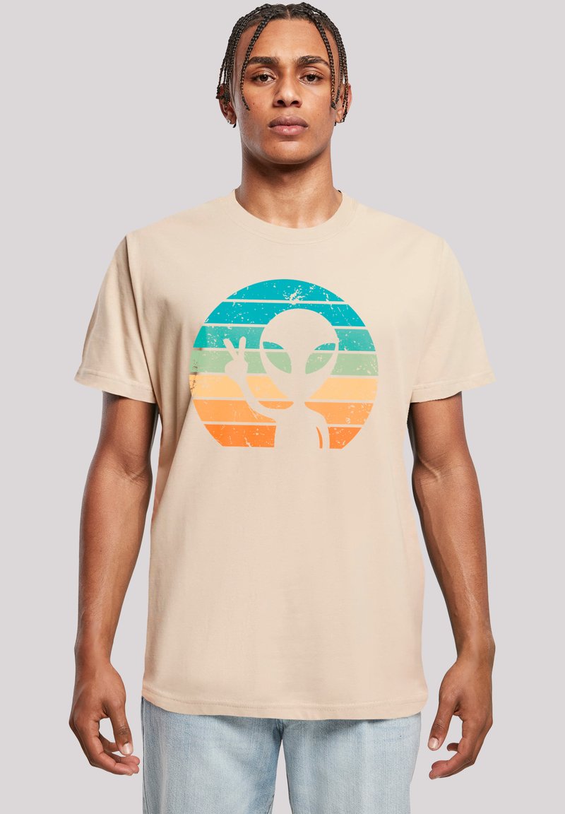 Beige cotton t-shirt featuring a distressed alien graphic in teal, orange, and blue circular design, with a peace sign. Short sleeves, relaxed fit.