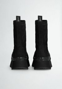 Stivaletti neri in suede, con tacco spesso e una fascia decorativa nera con un motivo attorno al metatarso.