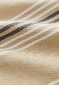 Beige kangas, jossa on vaalean ja tumman harmaan vaakasuoria raitoja; teksturoitu neulos, joka näyttää pehmeältä, hieman ryppyiseltä taitetusta asennosta.