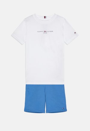 Camiseta de algodón blanca con el logo de "TOMMY HILFIGER", combinada con shorts de algodón azules. Los shorts tienen un pequeño acento del logo cerca del dobladillo.