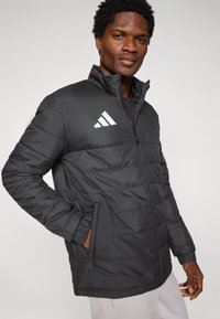 Μαύρο μπουφάν τύπου puffer με φερμουάρ μπροστά και ελαστικά μανίκια. Διαθέτει λευκό λογοτύπο με διαγώνιες ρίγες στο αριστερό στήθος και πλαϊνές τσέπες.