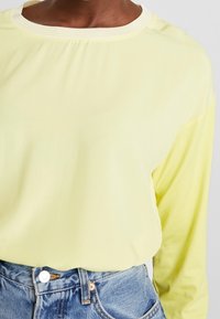 Langærmet top i pastellgul med ribbet rundhals. Stoffet er glat med let glans, kombineret med højtsiddende denim.