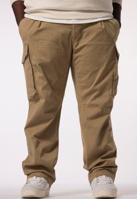Cargo pants in een lichte kaki kleur, met meerdere zakken en een relaxte pasvorm. Gemaakt van een gladde, lichte stof. Witte sneakers afgebeeld.