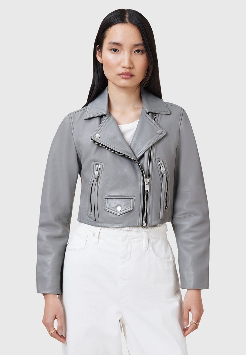 Giacca moto cropped in pelle grigia con colletto a rever, cerniera asimmetrica e tasche frontali con zip. Presenta una texture liscia e un design aderente.