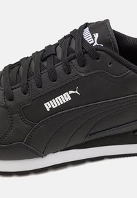 Czarne skórzane trampki o fakturowanym wykończeniu, z białym logo Puma, czarnymi sznurówkami i kontrastującą białą podeszwą.