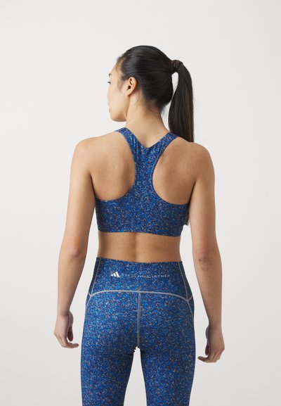 Sujeción deportiva azul y leggings de talle alto con un patrón texturizado y moteado. Presenta un diseño de espalda nadadora y acentos de hardware reflectante.