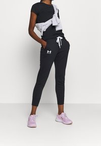 Svart T-shirt med korta ärmar, grå sweatshirt knuten runt axlarna, mörkgrå joggingsbyxor med vit dragsko och ljusrosa träningsskor.