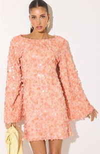 Femme en robe pêche à sequins avec de longues manches cloche, tenant une pochette jaune texturée, debout sur un fond blanc.