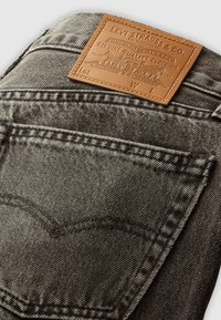 Achterzak en bruine leren patch van het merk Levi's op vervaagde zwarte denim jeans met zichtbare stikseldetails.