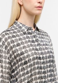 Chemise à motifs noir et blanc avec des dessins de sacs répétés sur un fond crème, avec un col et une texture douce.