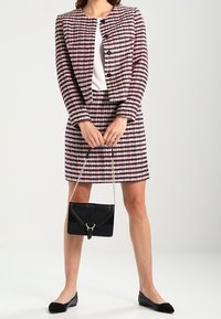 Completo a due pezzi in tessuto testurizzato con motivi a quadri rosa, neri e bianchi, abbinato a una borsa a tracolla nera e ballerine nere.