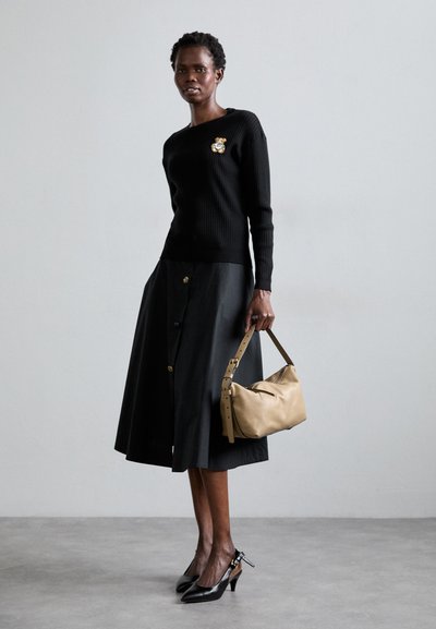 Pull noir côtelé avec une broche décorative, associé à une jupe midi noire à boutons. Un sac à épaule beige et des escarpins noirs à bout pointu complètent le look.