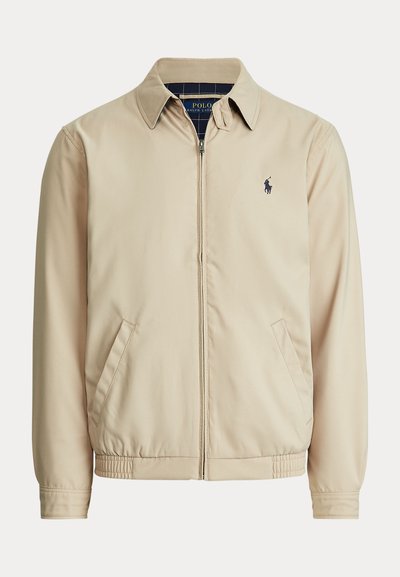 Beige jakke med lynlås, krave, sidelommer, elastisk talje og et lille mørkt Polo Ralph Lauren-logo på venstre bryst.
