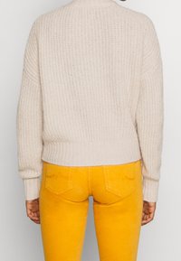 Maglione lavorato a maglia beige chiaro con orlo a coste, vestibilità oversize e maniche lunghe, abbinato a jeans gialli aderenti con tasche posteriori.