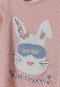 Un tessuto rosa a pois presenta un coniglietto bianco con orecchie a fantasia floreale, una maschera da sonno blu e il testo ricamato "BUONA NOTTE! DOLCI SOGNI!"