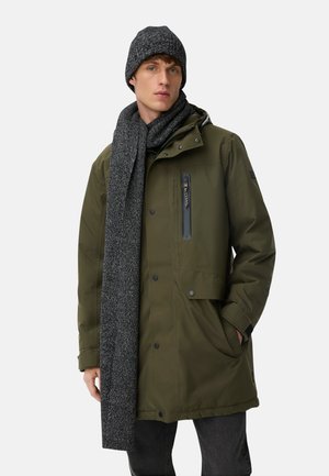 Olivgrüne wasserdichte Jacke mit Kapuze und Frontreißverschluss-Tasche, kombiniert mit einer grauen gestrickten Mütze und einem Schal. Ein grauer strukturierter Schal hängt über der Jacke.