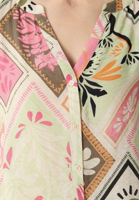 Koszula w wzory z dekoltem w serek i listwą guzikową. Kolory obejmują zieleń, róż, pomarańcz i brąz w florystycznych i geometrycznych wzorach.