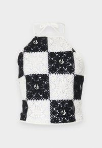 Top halter in crochet bianco e nero con motivo a scacchi, caratterizzato da motivi decorativi e chiusura a cravatta al collo.