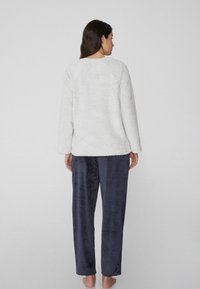Suéter de color gris claro, suave y texturizado, con mangas largas, combinado con pantalones de pijama de color azul oscuro, acanalados, con costuras visibles y detalle en la cinturilla.