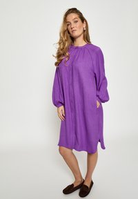 Lila knielanges Kleid mit rundem Ausschnitt, Ballonärmeln und Seitentaschen aus strukturiertem Stoff, mit lockerem Schnitt.