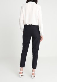 White blouse with long sleeves, black slim-fit pants, and white high-heeled sandals. The blouse has a relaxed fit; pants feature back pockets.
