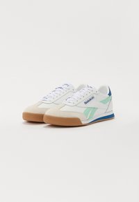 Bílé sneakers s světlými zelenými a modrými akcenty, semišovou špičkou a hnědou gumovou podrážkou. Šňůrky a branding na straně v modré barvě.