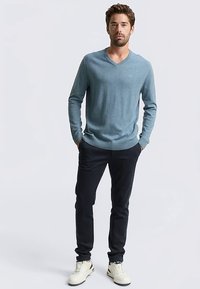 Lichtblauwe V-hals trui van zachte brei, gecombineerd met donkere broek en witte sneakers. De trui heeft een losse pasvorm. Geen zichtbare patronen.