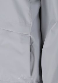 Hellgrauer Stoff mit sichtbaren Nähten und Steppdetails, zeigt eine Nahaufnahme der Verarbeitung und Textur eines Kleidungsstücks.