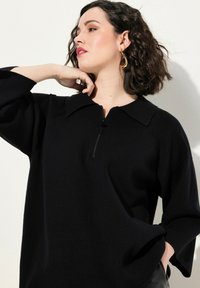 Maglione nero a pullover con colletto con zip, caratterizzato da una vestibilità ampia e una sottile texture a coste. Maniche lunghe con spalle abbassate.