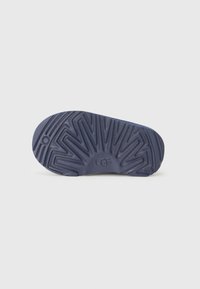 Semelle en caoutchouc marine avec un motif texturé et le logo UGG, conçue pour l'adhérence avec un bord incurvé et une légère indentation.