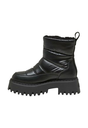 Personne portant une doudoune olive, une jupe plissée noire, des chaussettes grises et des bottes noires, debout à côté d'une porte de voiture ouverte sur un trottoir.