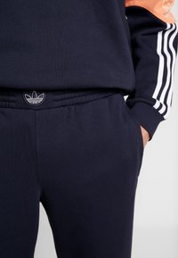 Marina-blå sweatpants i bomullsmix, med elastisk midja, sidofickor och tre vita ränder längs sidorna, samt logotypdetalj.