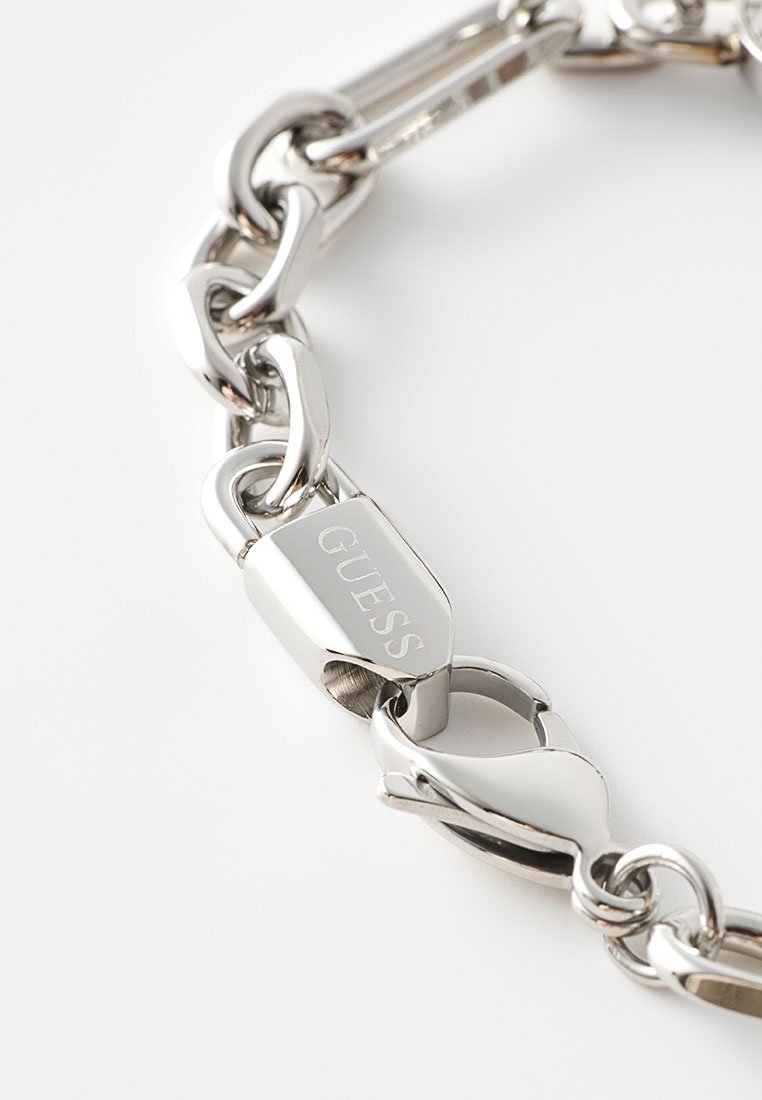 Bracelet en chaîne argentée avec de grands maillons, une finition polie et un fermoir portant le nom de la marque gravé "GUESS".