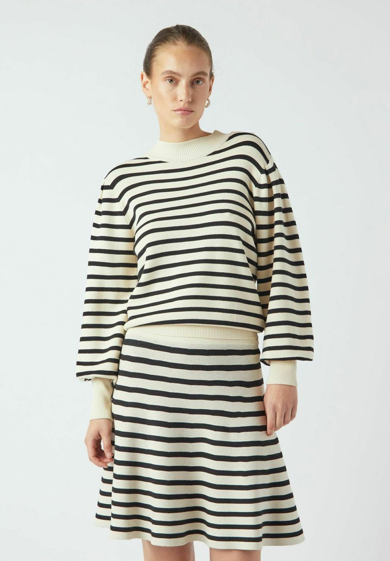 Kerman ja musta raitaneulepaidassa on leveät hihat, yhdistettynä yhteensopivaan liehuvaan hameeseen. Pehmeä tekstuuri ja ribattua hihansuita sekä helmaa.