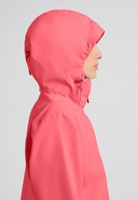 Giacca impermeabile rosa con cappuccio aderente. La texture liscia, le cuciture minime e gli elementi regolabili evidenziano funzionalità e protezione.
