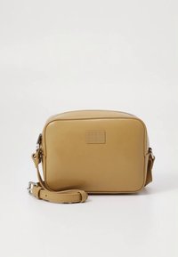 Bolso bandolera de cuero color tan con forma rectangular, cierre de cremallera, correa ajustable y logotipo en relieve en el frente. Textura lisa.