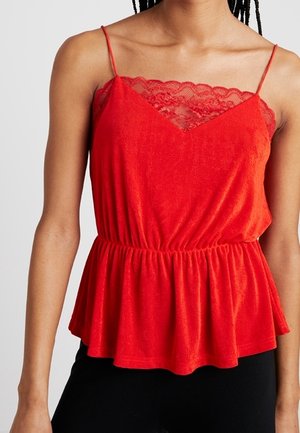 Rode mouwloze top met kanten halslijn, dunne bandjes, getailleerde taille en uitlopende zoom, gedragen met zwarte onderkleding.