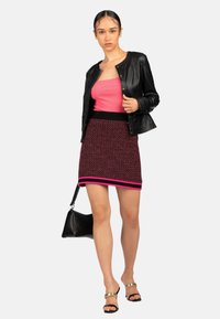 Giacca di pelle nera, top rosa senza maniche, gonna rosa e nera a fantasia con orlo a righe, sandali con dettagli dorati e borsa nera.