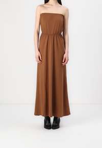 Bezramienna, brązowa maxi sukienka z elastycznym górą, ściągniętą w talii i zwiewnym krojem, w połączeniu z czarnymi, wysokimi botkami.