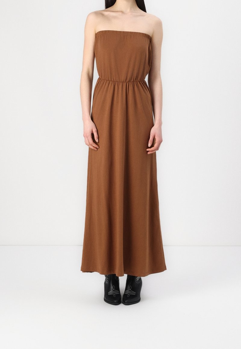 Bezramienna, brązowa maxi sukienka z elastycznym górą, ściągniętą w talii i zwiewnym krojem, w połączeniu z czarnymi, wysokimi botkami.