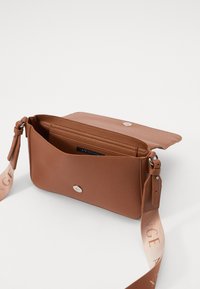 Brun lærcrossbody-veske med teksturert overflate, sølvfarget hardware og en avtakbar stropp med gradientdesign. Glidelås hovedrom.