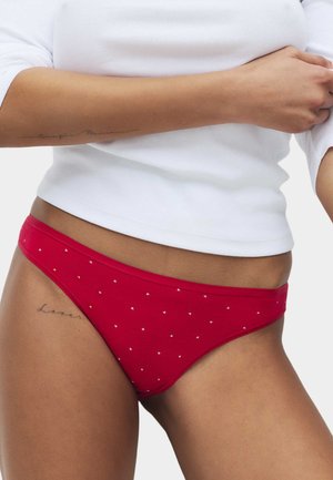 Bikini rosso in cotone con piccoli motivi a cuoricini bianchi, taglio a vita bassa, texture liscia e design leggero, abbinato a un top bianco a coste.