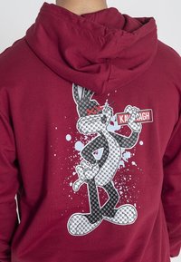 Felpa color bordeaux con cappuccio, caratterizzata da una stampa grafica di un coniglio dei cartoni, dettagliata con uno sfondo testurizzato e accenti di spruzzi bianchi.