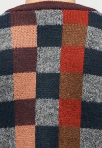 Κοντινό πλάνο πολύχρωμου πλεκτού πουλόβερ με κάθετο και οριζόντιο καρό σχέδιο σε αποχρώσεις του κόκκινου, καφέ, γκρι, μαύρου και ροδακινί.