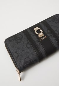 Black guess wallet featuring a textured exterior with a gold logo accent, a smooth black band, and a zip closure.