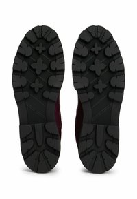 Un par de suelas negras de goma con dibujos profundos y patrones en cruz, que muestran el logo de Tommy Hilfiger en cada suela.