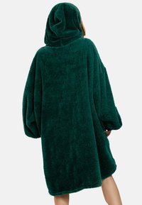 Robe oversize con cappuccio di colore verde scuro, realizzato in tessuto morbido e strutturato. Presenta maniche ampie e una vestibilità rilassata, che arriva fino a metà coscia.