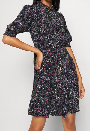 Šaty s květinovým potiskem, krátkými nafouklými rukávy, límečkem a rozšířeným lemem. Tmavě modré pozadí s barevnými květinami a lehká látka.